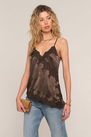 A woman modeling a brown lace-trimmed camisole top with a satin sheen, paired with light-wash blue jeans, against a solid light beige background.
