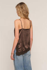 A woman shown from the back wearing a dark brown satin camisole top with thin straps and a distressed, frayed hem, paired with light blue jeans, against a plain light beige background.