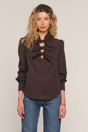 A woman wearing a dark brown and black checkered blouse with a large ruffled keyhole neckline