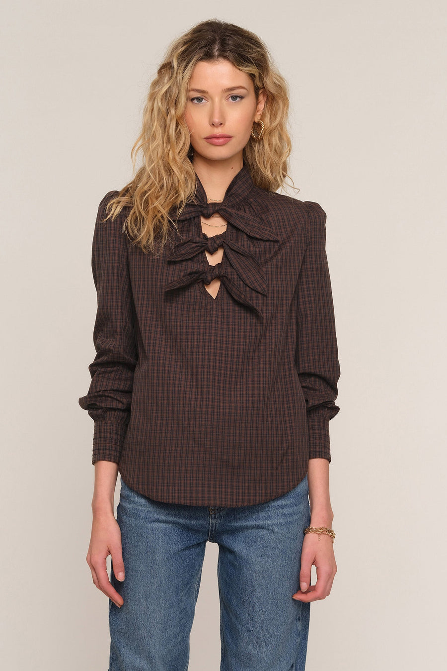 A woman wearing a dark brown and black checkered blouse with a large ruffled keyhole neckline