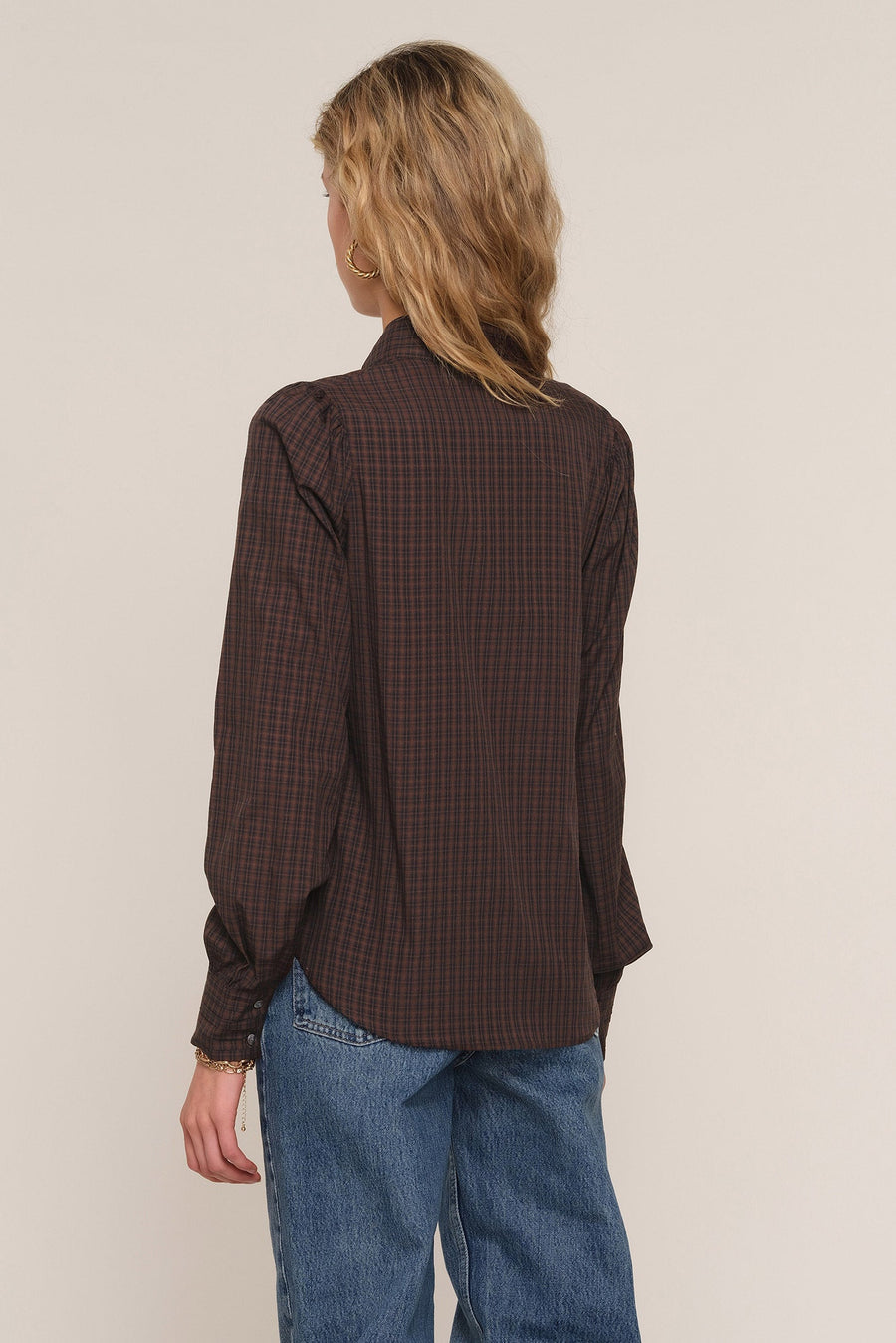 A woman shown from the back wearing a dark brown and black checkered long-sleeve button-up 