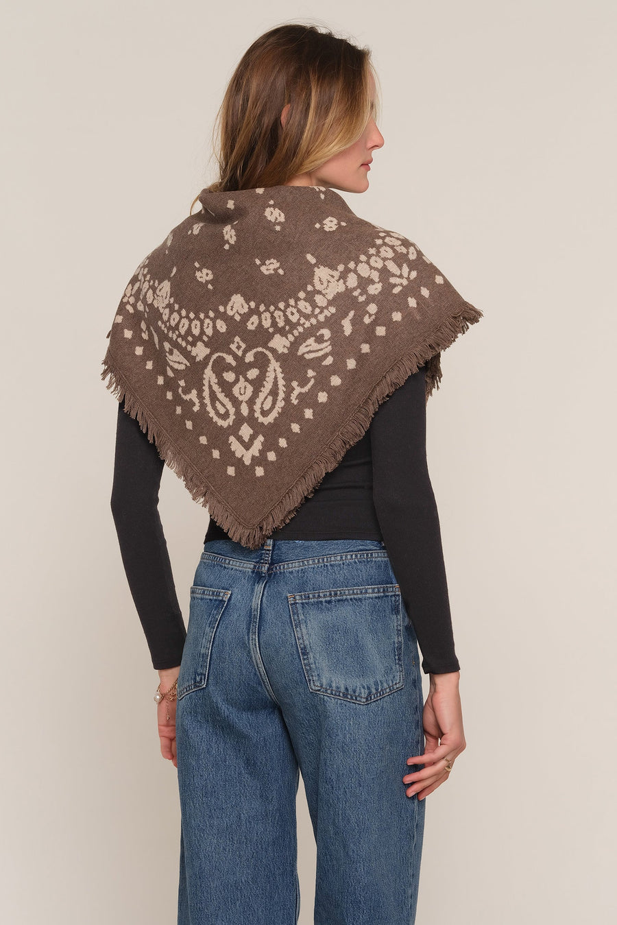 A woman shown from the back wearing a brown shawl with a cream paisley and floral pattern 