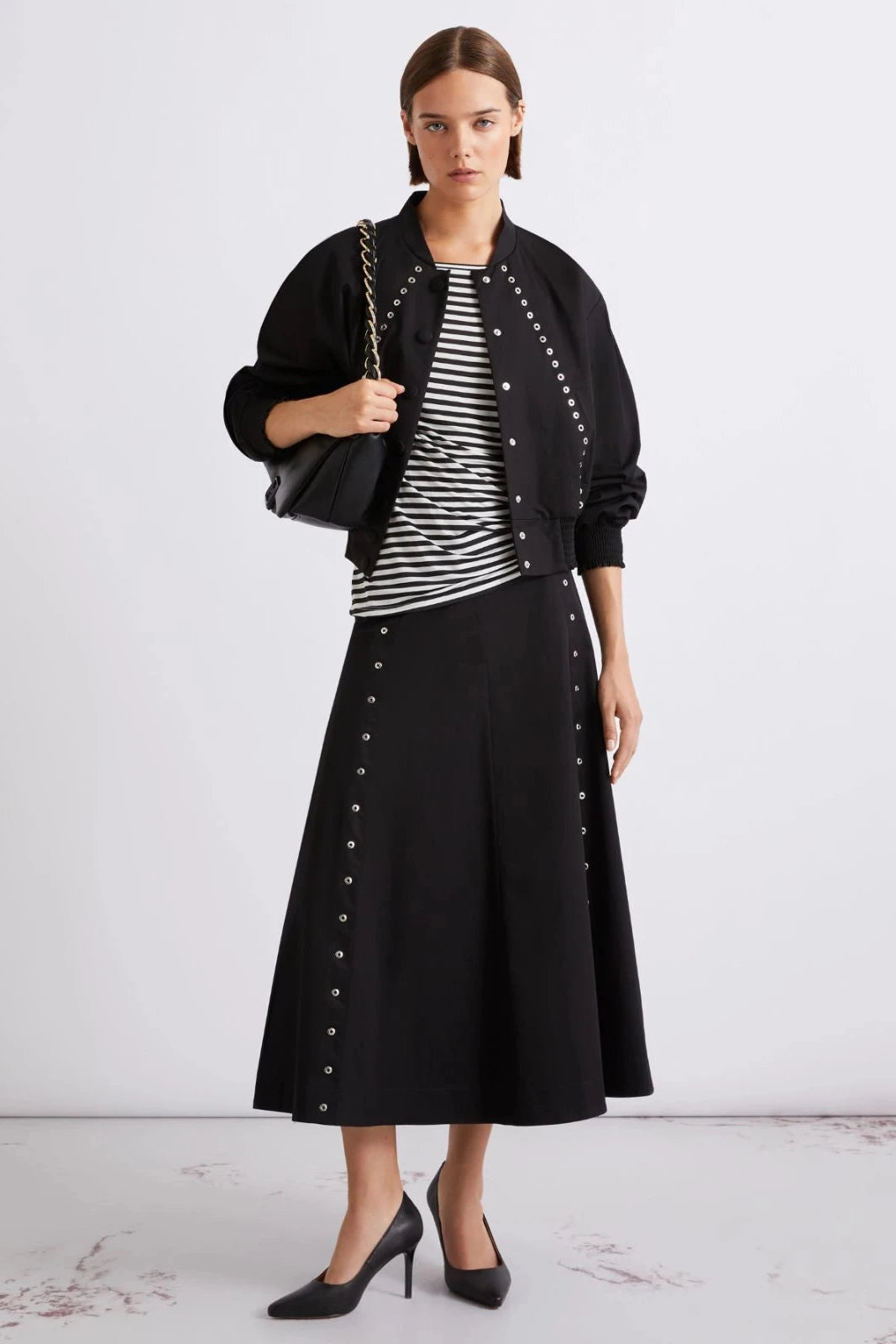 Woman wearing a black midi skirt with metal button detail