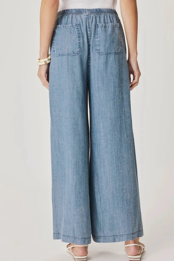 Back view of Woman wearing a pair of indigo flowy pants With drawstring waistband