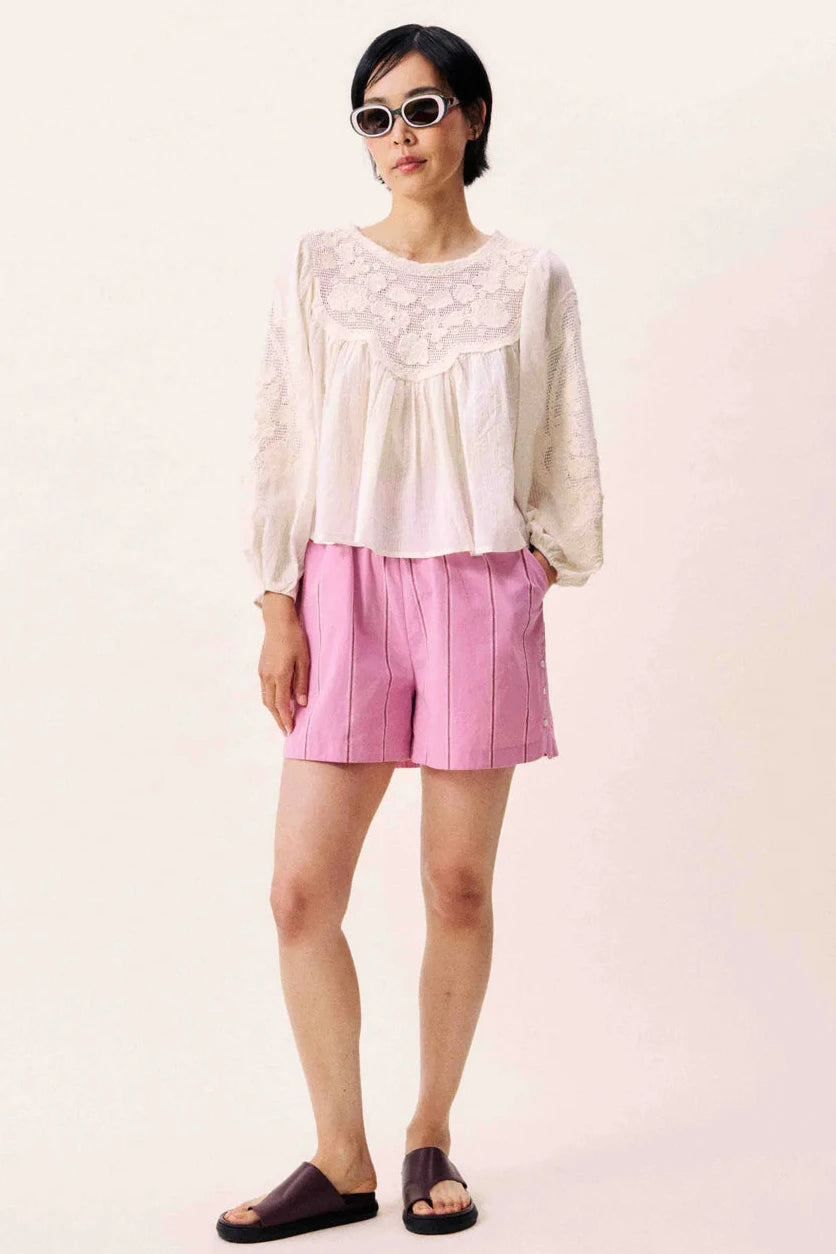 Woman wearing a white cream colored blouse with a open black and embroidered details 