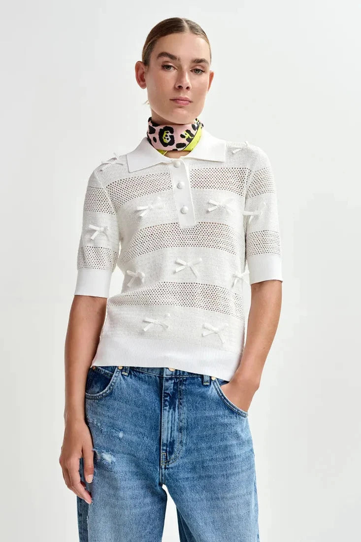 Woman wearing a white knit polo with little bow details all over 