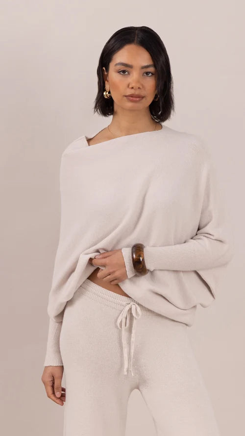 Woman wearing a beige sweater and pants set against a plain background