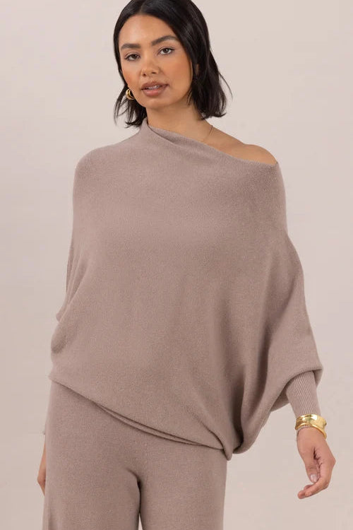 Woman wearing a beige off-shoulder top and pants against a plain background