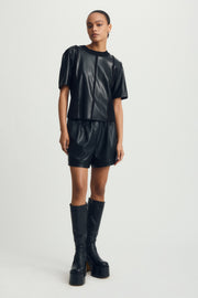 Person wearing a black leather outfit with shorts and knee-high boots on a white background