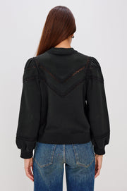 woman wearing a black sweatshirt with lace detailing and cuffed poplin  sleeves
