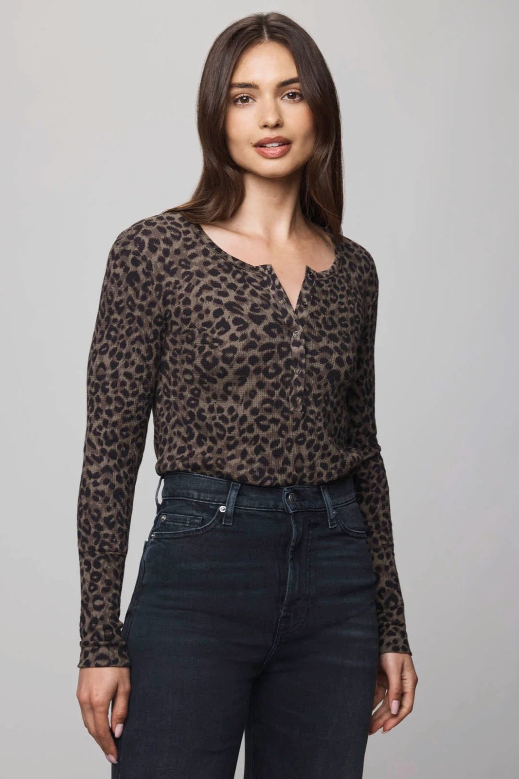 Woman wearing a leopard print long-sleeve top and dark jeans against a gray background