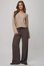 Woman wearing a beige sweater and brown pants on a gray background