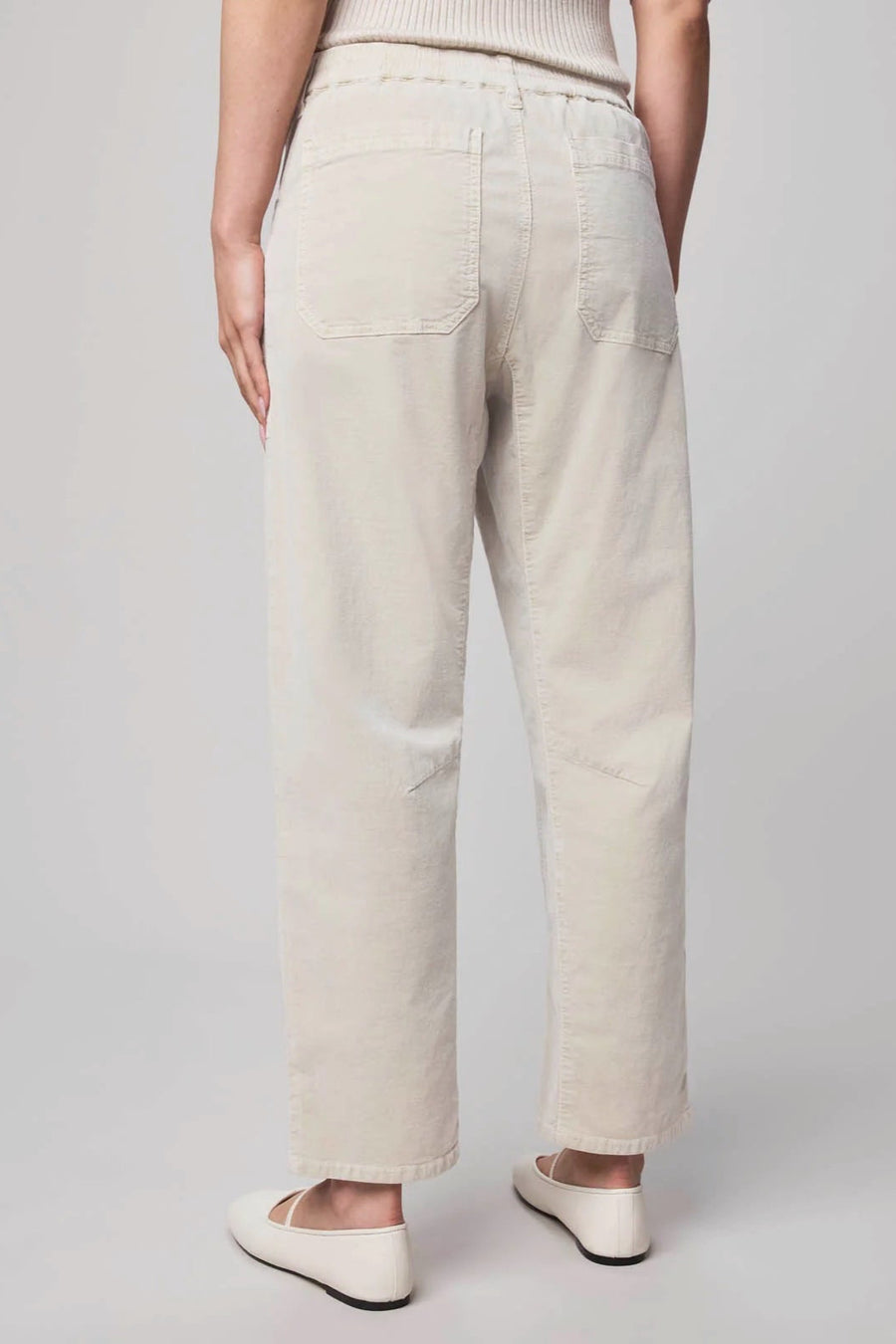 Back view of a person wearing oat-coloured corduroy pants and white sneakers on a plain background
