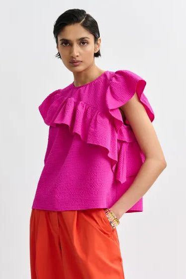 Woman wearing a bright pink top with ruffled sleeves, front