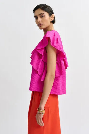 Woman wearing a bright pink top with ruffled sleeves, side