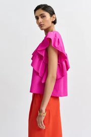 Woman wearing a bright pink top with ruffled sleeves, side