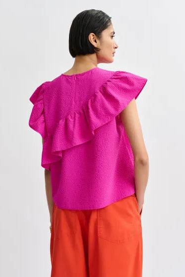 Woman wearing a bright pink top with ruffled sleeves, back