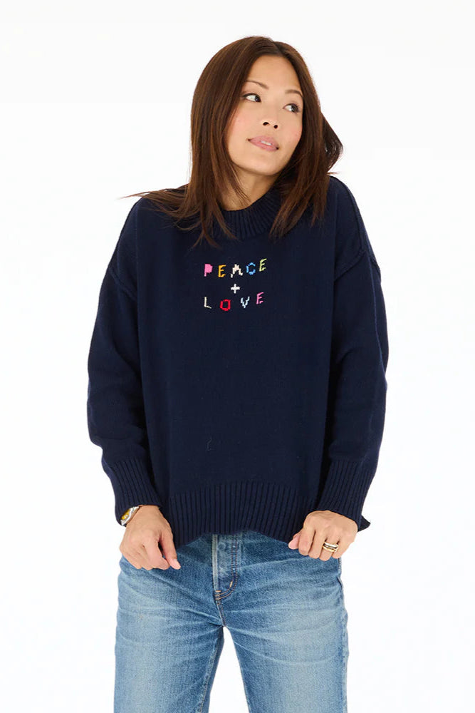 Front view of woman wearing navy blue mock-neck knitted sweater with "Peace + Love" embroidered