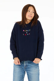 Front view of woman wearing navy blue mock-neck knitted sweater with "Peace + Love" embroidered