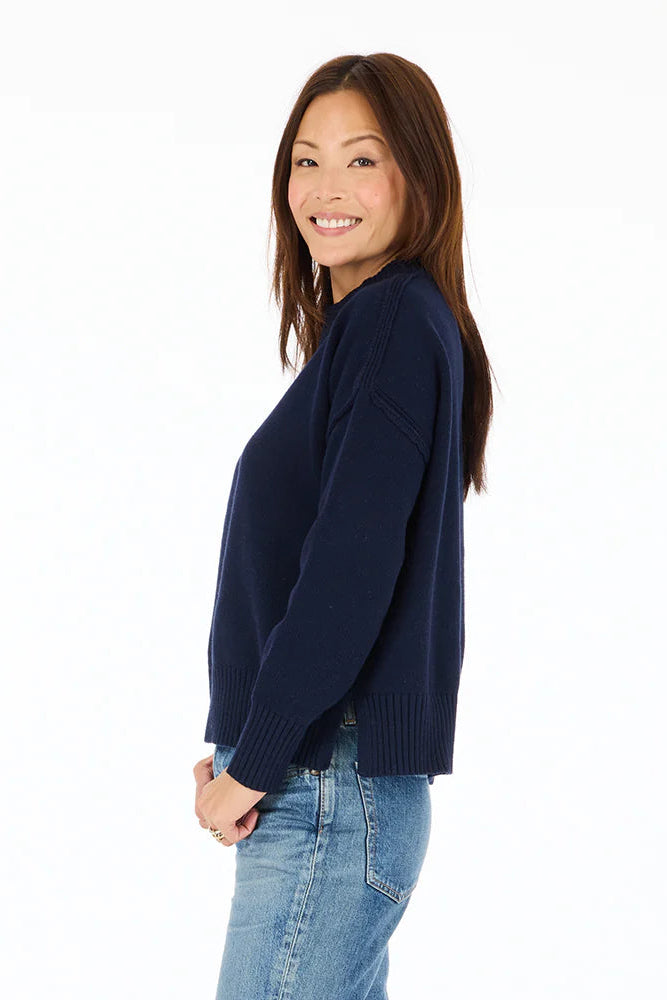 Side view of woman wearing navy blue mock-neck knitted sweater with "Peace + Love" embroidered
