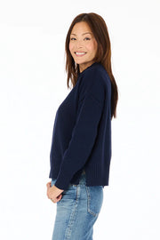 Side view of woman wearing navy blue mock-neck knitted sweater with "Peace + Love" embroidered