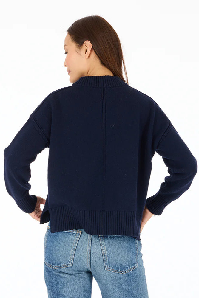 Back view of woman wearing navy blue mock-neck knitted sweater with "Peace + Love" embroidered