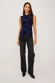 woman wearing a sleeveless navy mesh top with a pattern of black velvet roses and washed black denim jeans