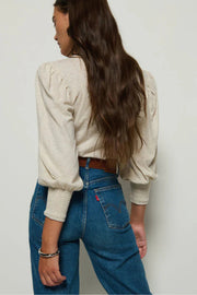 Person wearing a cream sweater and blue jeans against a plain background