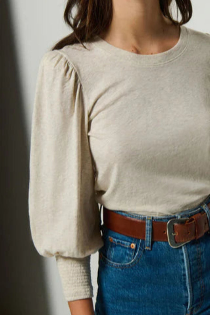 Woman wearing a beige long-sleeve top and blue jeans against a plain background