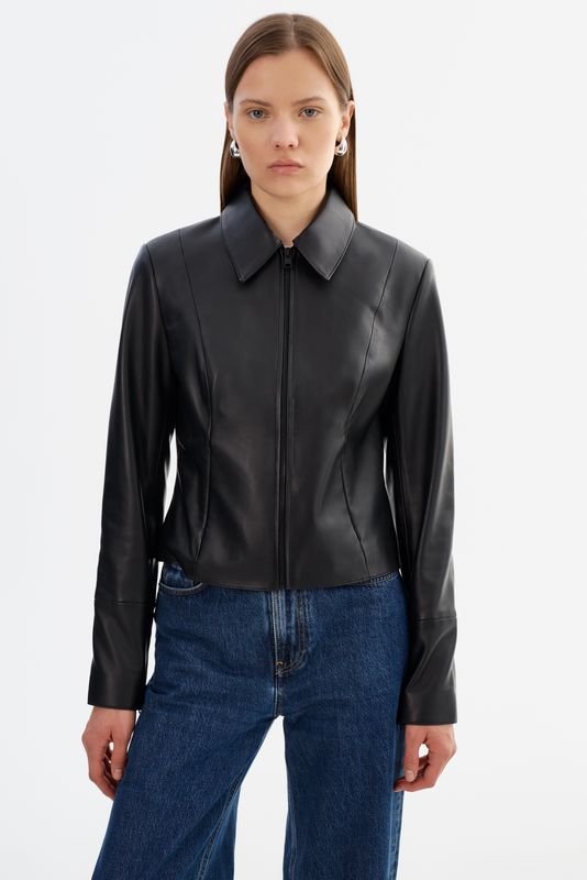 A woman modeling a black leather jacket with a pointed collar and front zipper, 