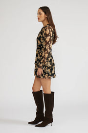 Side view of a woman wearing a mini black with beige flowers dress with long sleeves and knee-high boots
