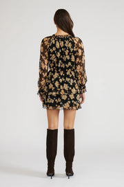 Back view of a woman wearing a mini black with beige flowers dress with long sleeves and knee-high boots
