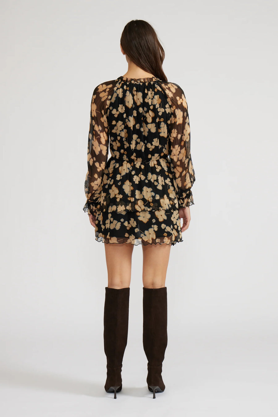 Back view of a woman wearing a mini black with beige flowers dress with long sleeves and knee-high boots