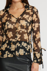 Close-up  view of a woman wearing a sheer long sleeve floral blouse with a black skirt on a white background