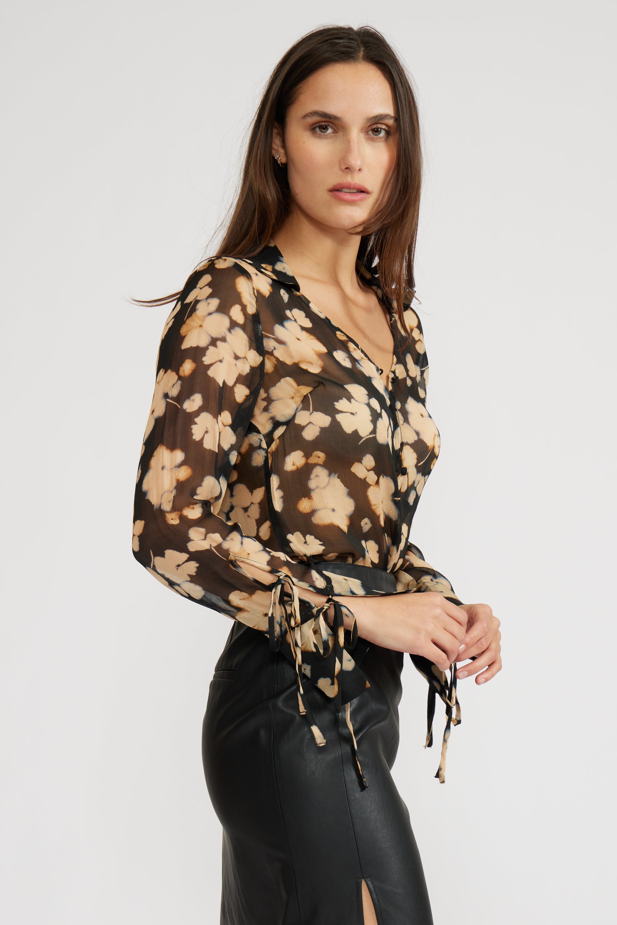 Side  view of a woman wearing a sheer long sleeve floral blouse with a black skirt on a white background
