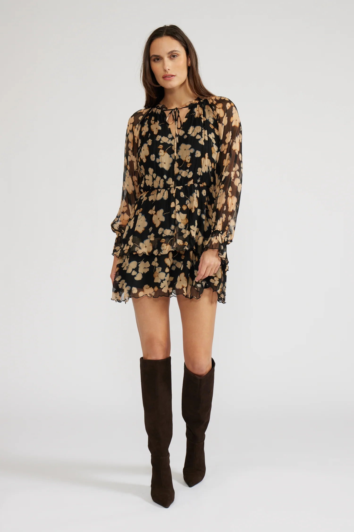 Front view of a woman wearing a mini black with beige flowers dress with long sleeves and knee-high boots