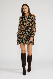 Front view of a woman wearing a mini black with beige flowers dress with long sleeves and knee-high boots