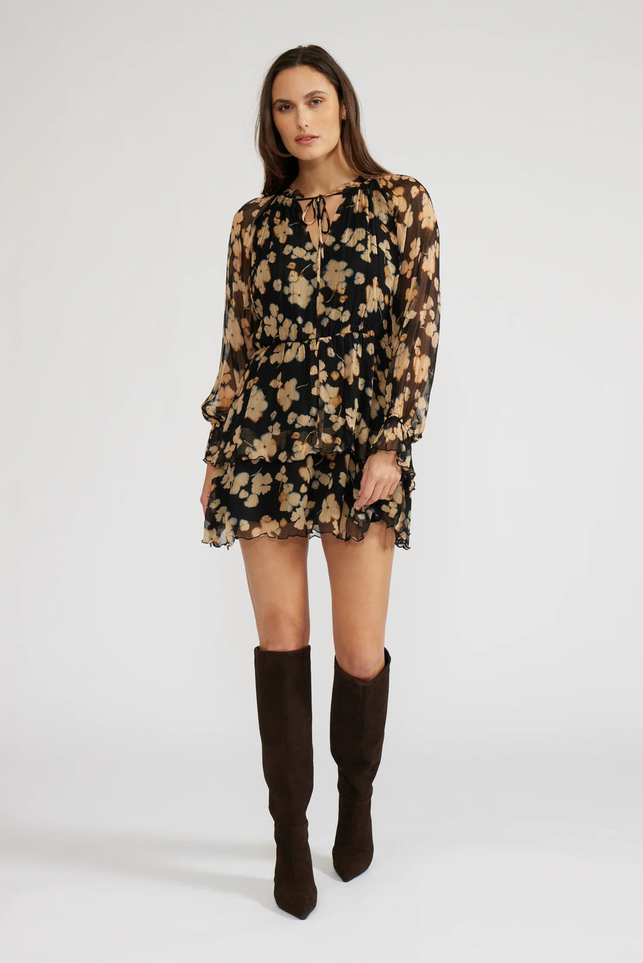 Front view of a woman wearing a mini black with beige flowers dress with long sleeves and knee-high boots