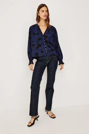 woman wearing a blue blouse with black roses and buttons and jeans