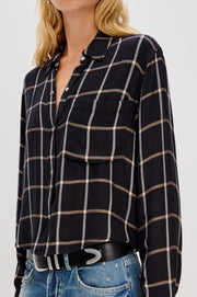 Close-up of a person wearing  a black and white plaid shirt and blue jeans on a light gray background