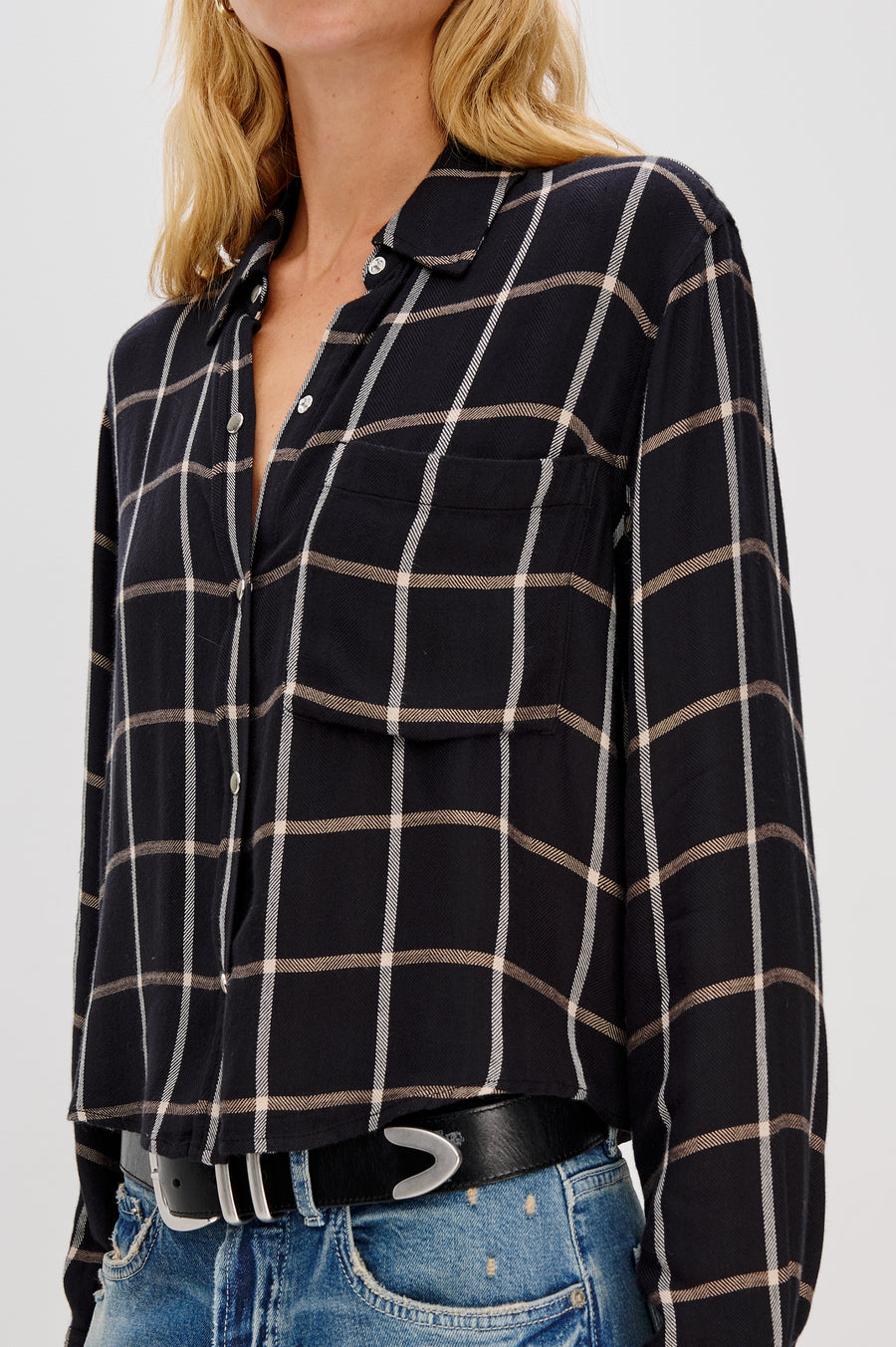 Close-up of a person wearing  a black and white plaid shirt and blue jeans on a light gray background