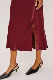 Maroon satin skirt with a high slit worn by a person on a white background