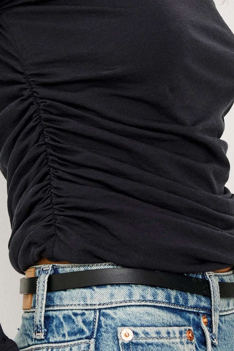 Person wearing a black long-sleeve top with ruched detail and blue jeans on a white background