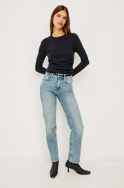 Woman wearing a black long-sleeve top and light blue jeans on a white background