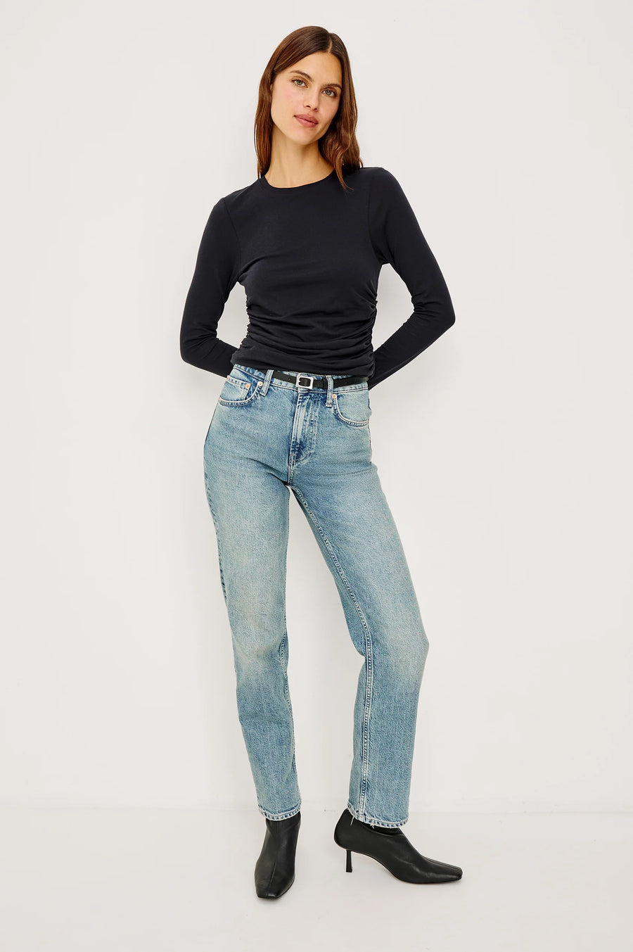 Woman wearing a black long-sleeve top and light blue jeans on a white background