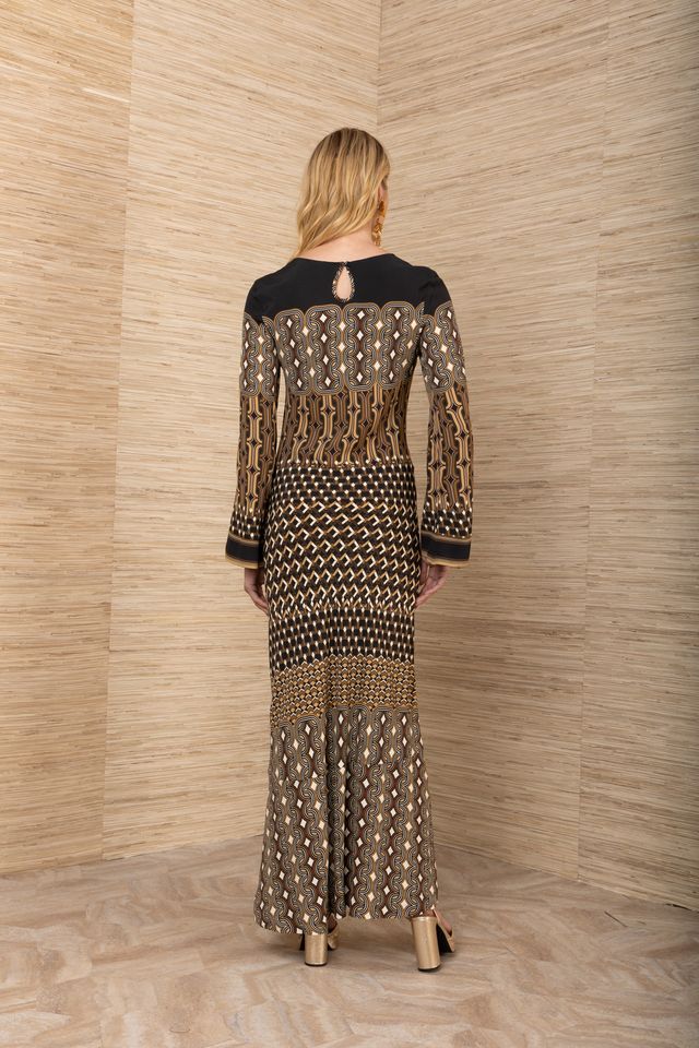 Back view of woman wearing a black, brown and mustard yellow patterned maxi jersey long sleeve dress.