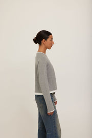 A model wearing a grey long-sleeve crewneck sweater with white ribbed trim at the collar, cuffs, and hem. 