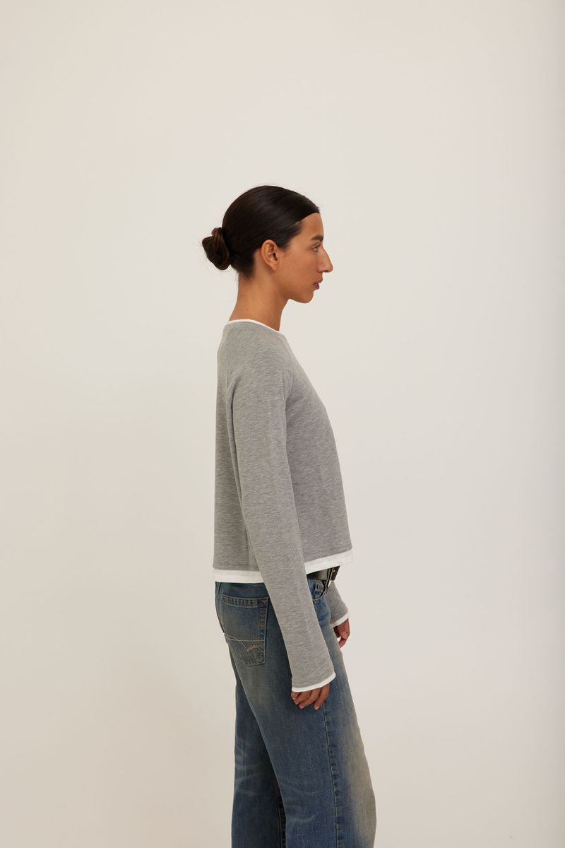 A model wearing a grey long-sleeve crewneck sweater with white ribbed trim at the collar, cuffs, and hem. 