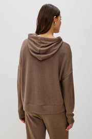 Back view of a woman wearing a matching set of light brown hoodie and pants on a white background