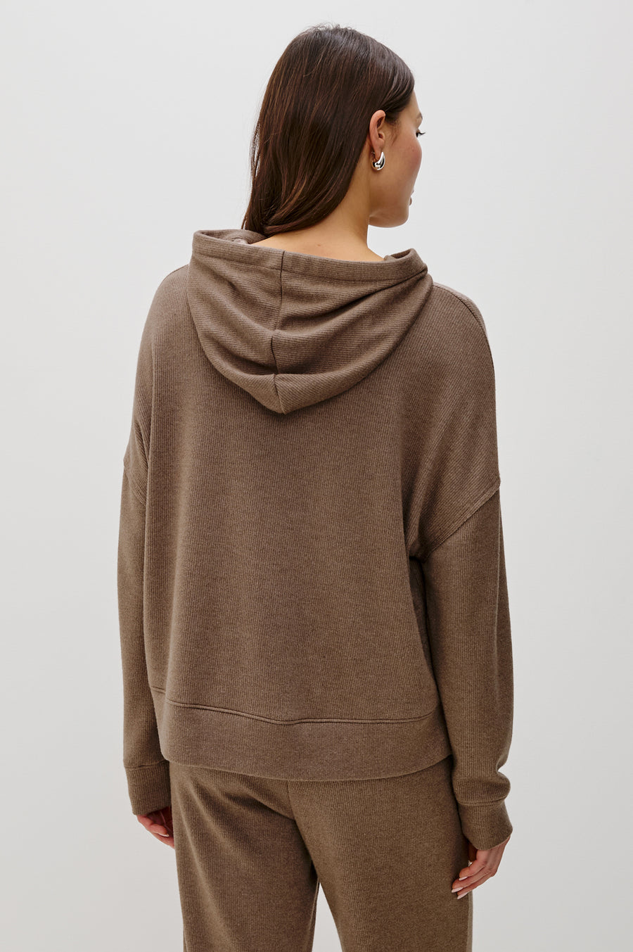 Back view of a woman wearing a matching set of light brown hoodie and pants on a white background